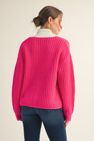 Person wearing a bright pink sweater and blue jeans on a beige background