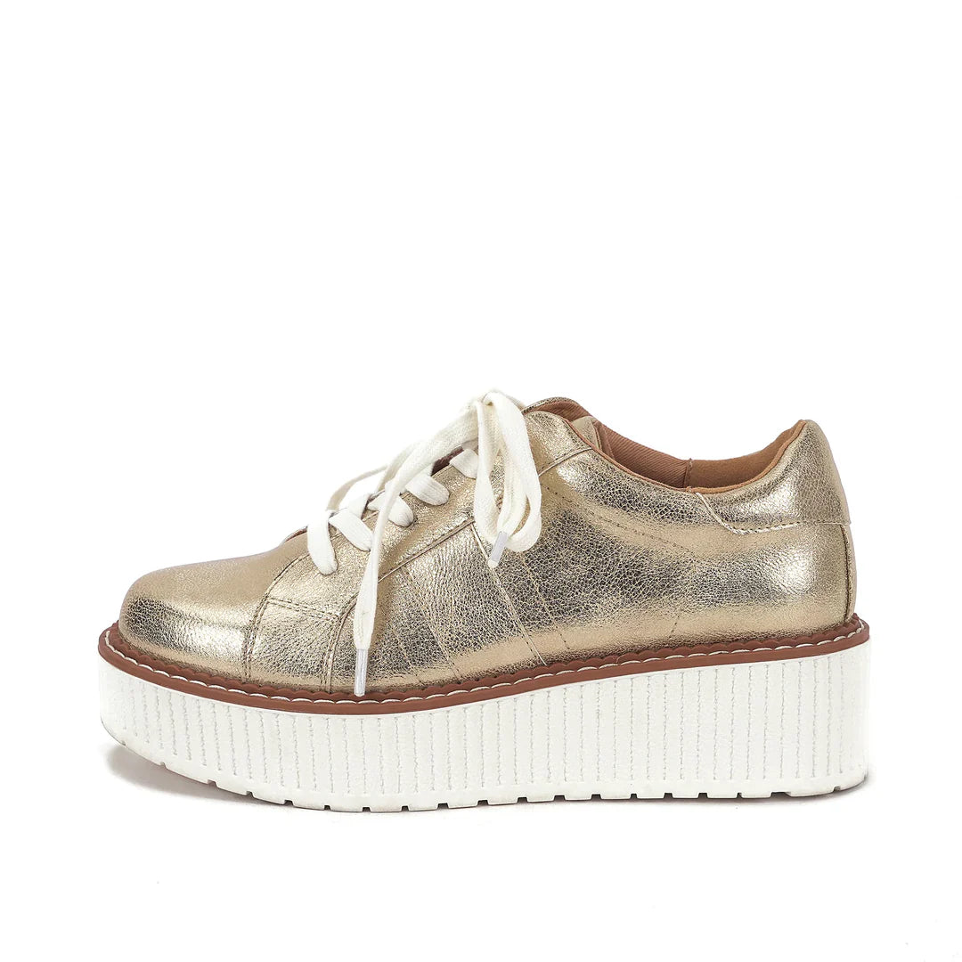 Light gold metallic lace-up flatform sneaker with a textured white platform sole photographed on a white background.