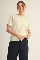 odel wearing a short-sleeve sequin top with a soft shimmer finish, paired with black wide-leg pants and ankle boots. The look is elegant, minimal, and perfect for a polished festive outfit.