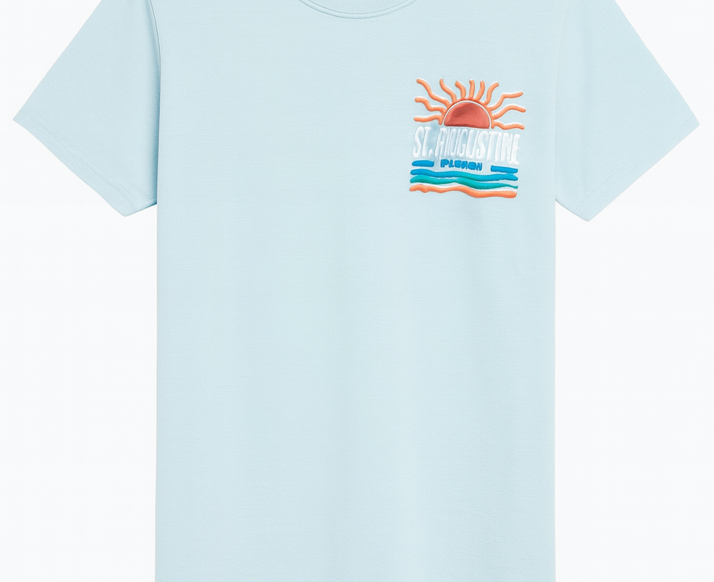 Light blue St. Augustine Florida T-shirt featuring a bold retro sun and ocean waves design in orange, teal, and white. Soft cotton fabric with vibrant raised print celebrating Florida’s coastal charm — exclusive to Artsy Abode.