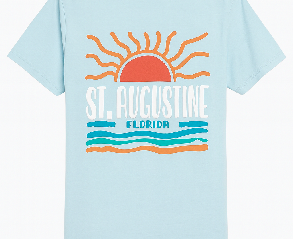 Light blue St. Augustine Florida T-shirt featuring a bold retro sun and ocean waves design in orange, teal, and white. Soft cotton fabric with vibrant raised print celebrating Florida’s coastal charm — exclusive to Artsy Abode.