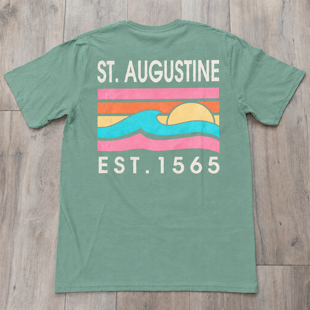 Back of magenta St. Augustine t-shirt with retro sunset stripe graphic, turquoise wave design, and “ST. AUGUSTINE EST. 1565” text.
