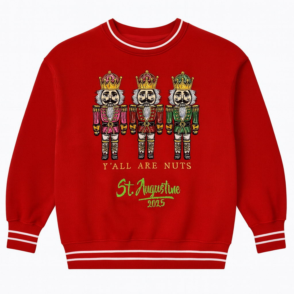 Red holiday sweatshirt featuring three embroidered nutcrackers with the text “Y’all Are Nuts St. Augustine 2025,” accented with white striped cuffs and collar for a festive seasonal look.