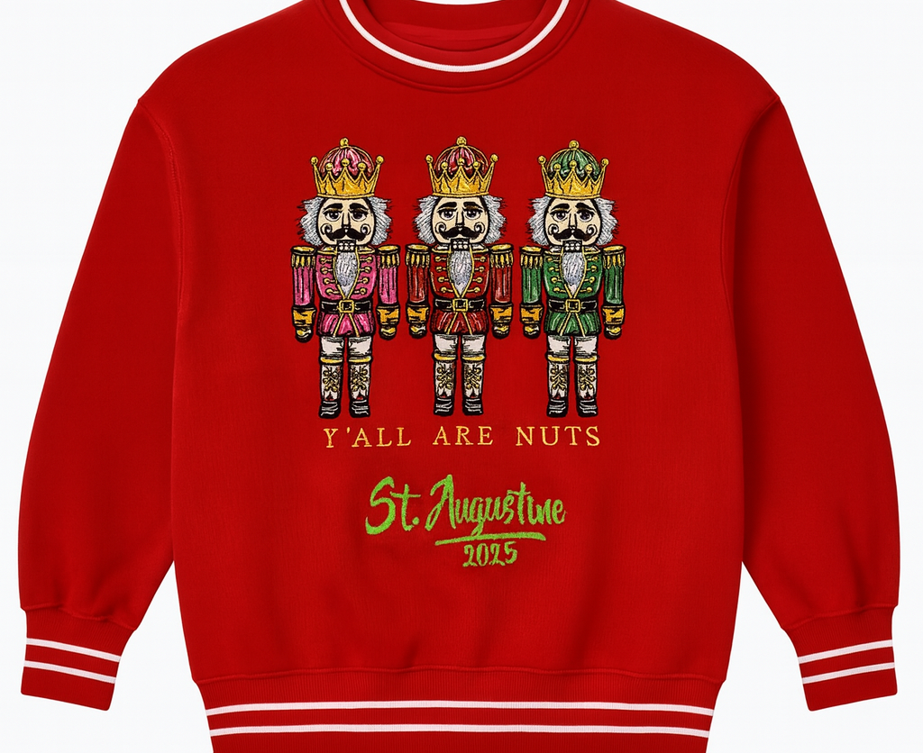 Red holiday sweatshirt featuring three embroidered nutcrackers with the text “Y’all Are Nuts St. Augustine 2025,” accented with white striped cuffs and collar for a festive seasonal look.