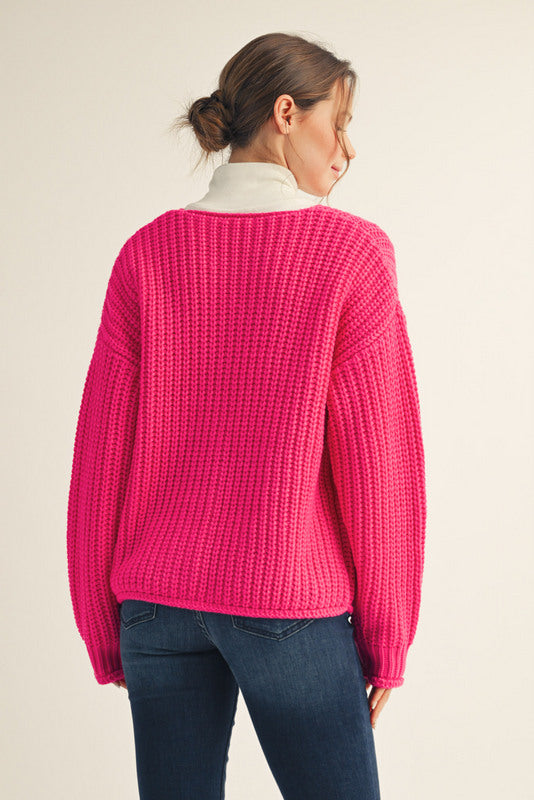 Person wearing a bright pink sweater and blue jeans on a beige background