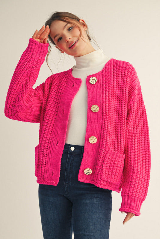 Woman wearing a bright pink cardigan with gold buttons on a plain background