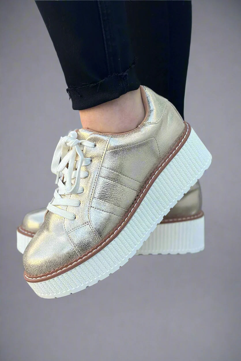 Light gold metallic lace-up flatform sneaker with a textured white platform sole photographed on a white background.