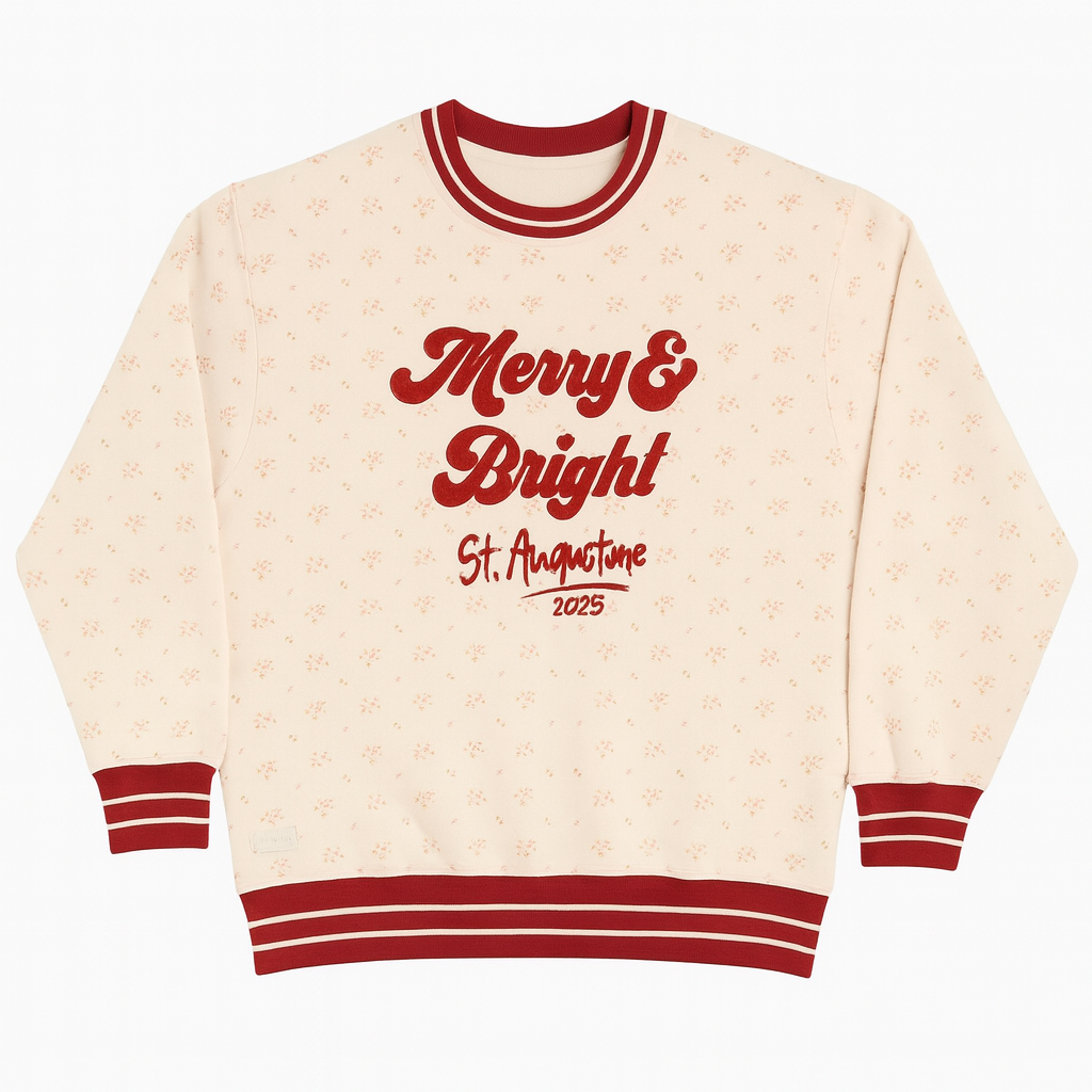 Light pink holiday sweatshirt with red “Merry & Bright St. Augustine 2025” embroidery, red striped cuffs and collar, and a subtle floral pattern—festive cozy style perfect for the holidays.