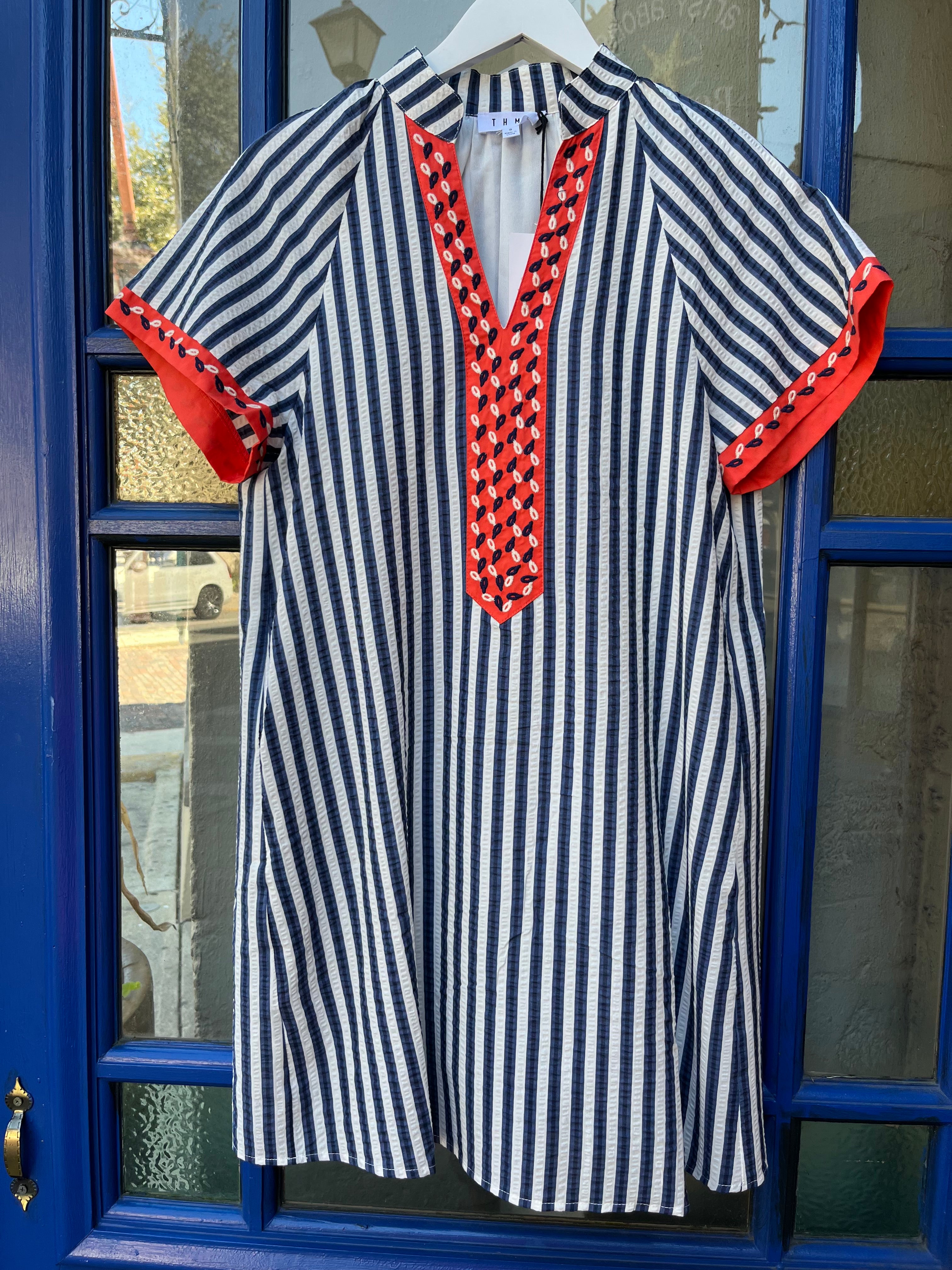 Navy and white striped short sleeve dress with split V-neck collar and orange contrast placket and sleeve cuffs, hanging on a white hanger.