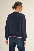 Model wearing a navy Christmas sweater with colorful tree patterns and a sparkling sequin tree in the center, paired with dark blue jeans — festive, cozy, and perfect for the holidays.