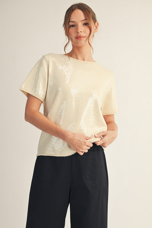 odel wearing a short-sleeve sequin top with a soft shimmer finish, paired with black wide-leg pants and ankle boots. The look is elegant, minimal, and perfect for a polished festive outfit.
