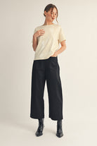 Model wearing a short-sleeve sequin top with a soft shimmer finish, paired with black wide-leg pants and ankle boots. The look is elegant, minimal, and perfect for a polished festive outfit.