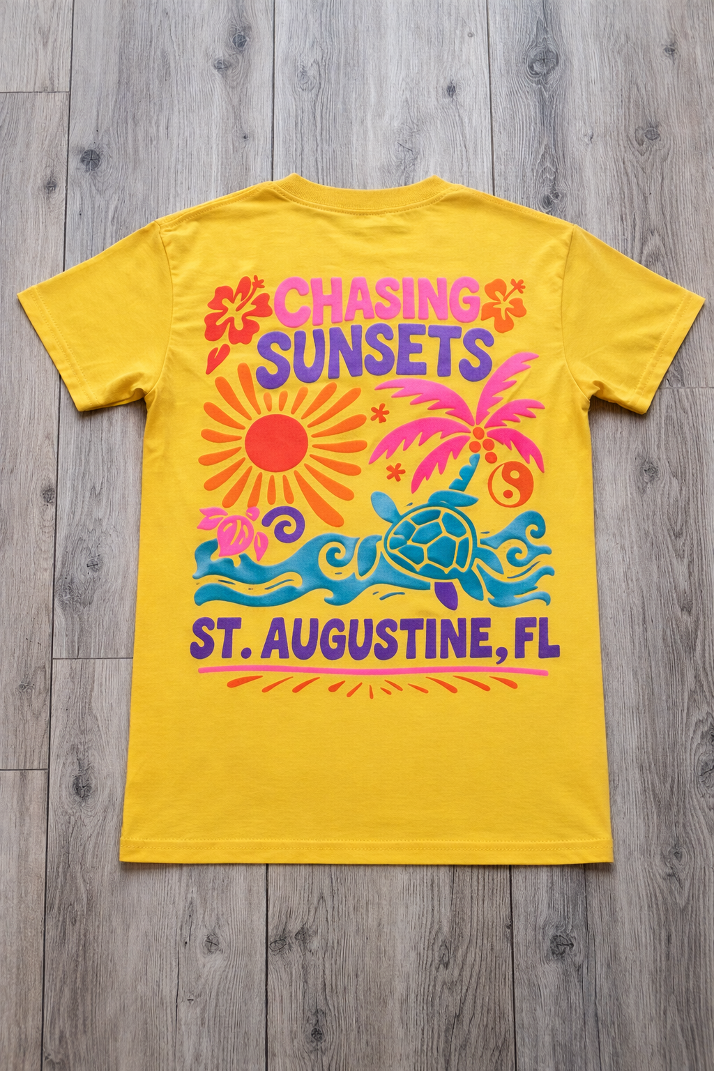 Back of yellow St. Augustine t-shirt with colorful “Chasing Sunsets” graphic featuring a sun, palm tree, waves, sea turtle, and St. Augustine, FL text.