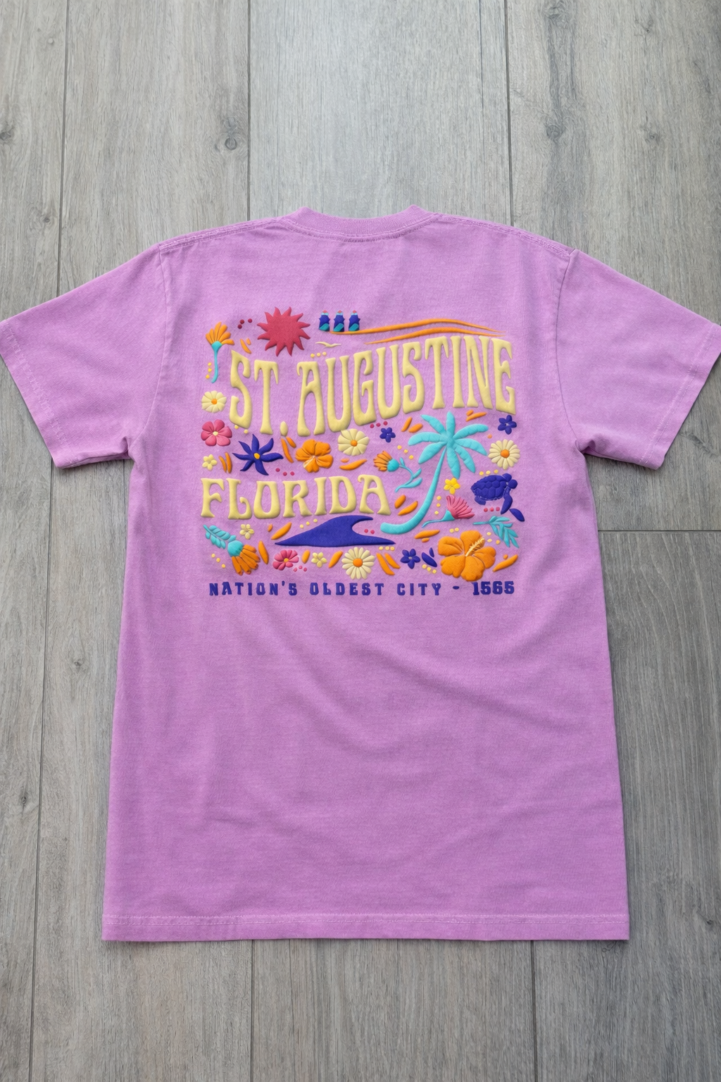Back of lavender St. Augustine Florida t-shirt with colorful tropical floral design, palm tree, sea turtle, and “Nation’s Oldest City - 1565” text.