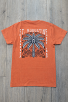 Back of orange St. Augustine t-shirt with large palm tree graphic, tribal-inspired artwork, and white “St. Augustine Florida Est. 1565” text.