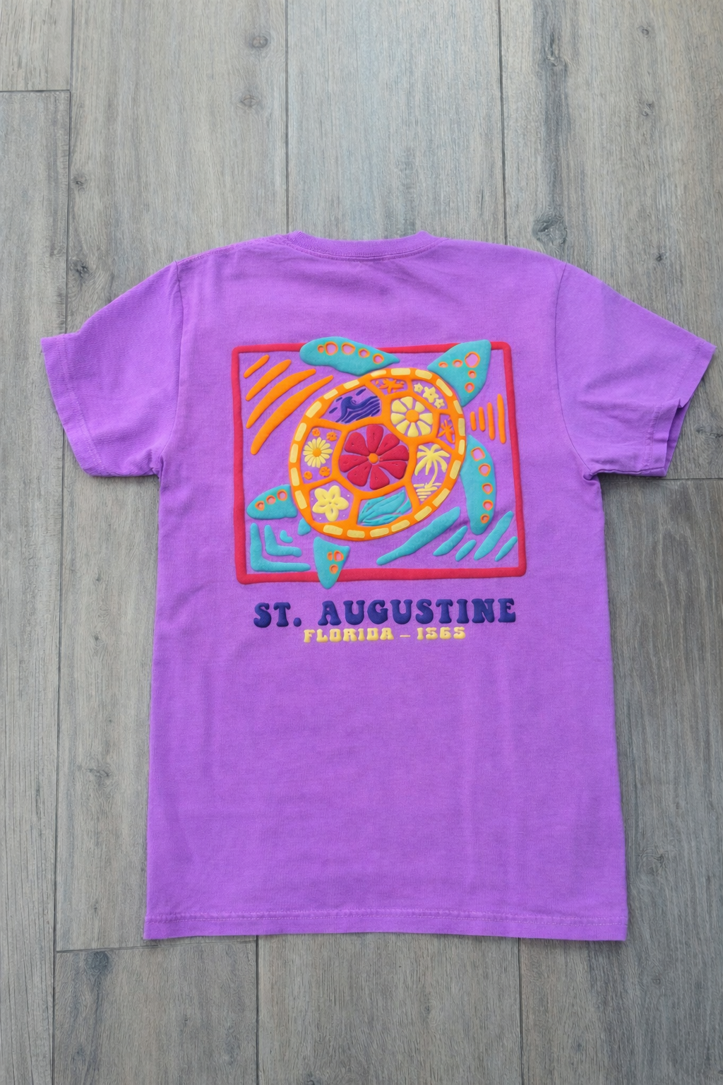 Back of purple St. Augustine t-shirt with colorful sea turtle graphic in a framed design and “St. Augustine Florida - 1565” text.